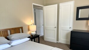 A hotel room with a bed, two doors, a nightstand with a lamp, and a dresser. - Cute and Cozy Near Parks (Midland)