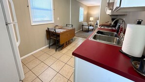 A compact kitchen with a red countertop, a dining area with a wooden table, and a window with blinds. - Cute and Cozy Near Parks (Midland)