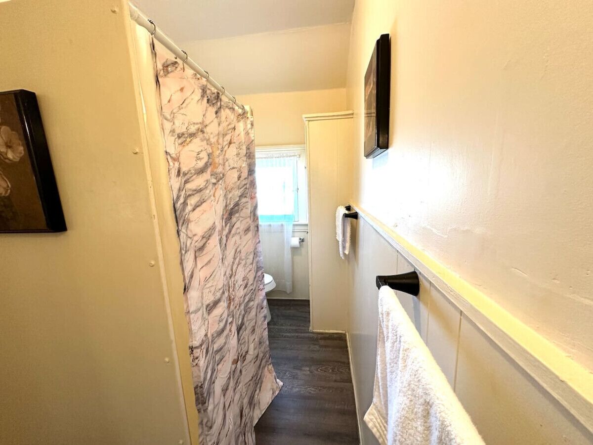 A narrow hallway with a marble-patterned shower curtain, a white door at the end, and a towel rack on the wall.