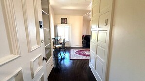 Un pasillo con puertas de paneles blancos, una zona de comedor con mesa y sillas, y una alfombra roja con estampado en el suelo.