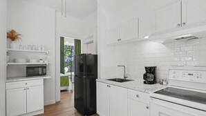 Una cocina moderna con armarios blancos, un refrigerador negro, una cafetera y un microondas.