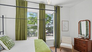 Una cama con dosel, cortinas verdes, una silla, un aparador y un cuadro en la pared.