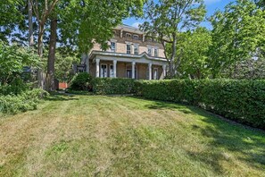 A two-story house with a front porch, surrounded by a well-maintained lawn and dense shrubbery. - Elizabeth`s Entire Apt @ Historic McCormick House (Bay City)