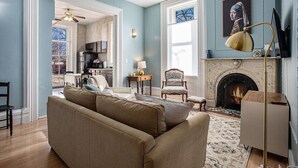 A living room with a beige sofa, a fireplace, and a television. - Elizabeth`s Entire Apt @ Historic McCormick House (Bay City)