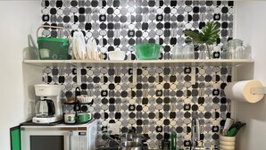 A kitchen with a microwave, coffee maker, and a sink. There are shelves above the counter holding various kitchen items. - Fun & Functional Studio Apt (Bay City)