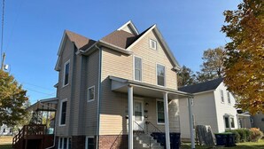 A two-story house with a front porch, a covered entryway, and a visible staircase leading to the second floor. - Fun & Functional Studio Apt (Bay City)
