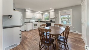 Una cocina moderna con armarios blancos, una mesa de comedor con sillas y una ventana con persianas.