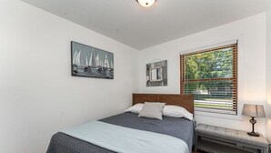Un dormitorio con cama, un banco, una ventana con persianas y un cuadro en la pared.