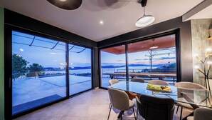 Un espace repas moderne avec une table et des chaises en verre, de grandes fenêtres donnant sur l’extérieur et un balcon doté d’une balustrade.
