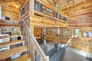 L’intérieur d’une cabane en rondins comprend un escalier menant à une chambre à l’étage, un espace de vie avec un canapé et un coin cuisine.