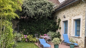A stone building with a garden patio featuring two blue lounge chairs and a white metal table. - Stone studio in the grounds of "La Closerie" guest house  (Droue-sur-Drouette)