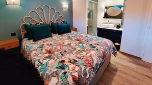 A bedroom with a bed featuring a floral-patterned bedspread, a wooden headboard, and two wall-mounted lights. - Stone studio in the grounds of "La Closerie" guest house  (Droue-sur-Drouette)