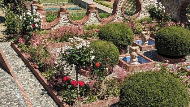A garden with a greenhouse, stone structures, and various plants. - Stone studio in the grounds of "La Closerie" guest house  (Droue-sur-Drouette)