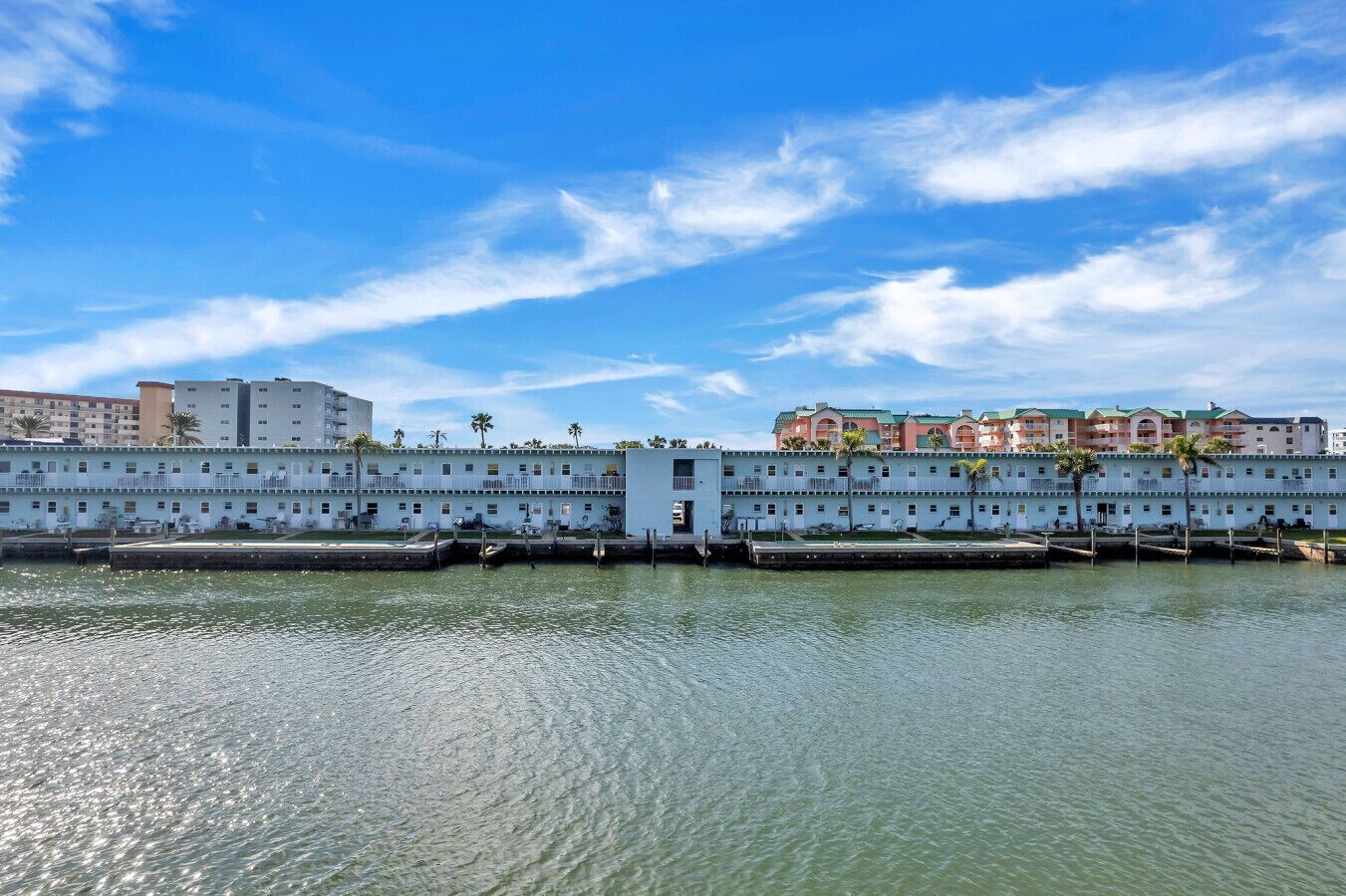 A waterfront hotel with multiple balconies, a dock, and a view of other buildings in the background.