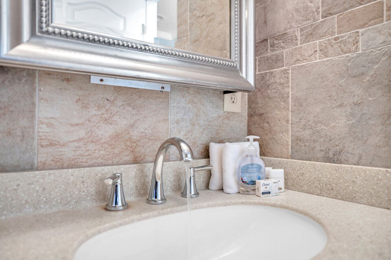 Une salle de bain avec un lavabo en marbre, deux robinets, un miroir et des articles de toilette.