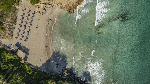 Vista aèria d'una platja amb filera de sombrerets i algunes persones.