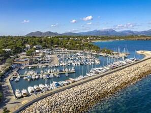 A marina with numerous boats docked, surrounded by a rocky breakwater and a backdrop of mountains and clear skies. - Villa Marilen · Villa with private pool in Alcúdia (Alcúdia)