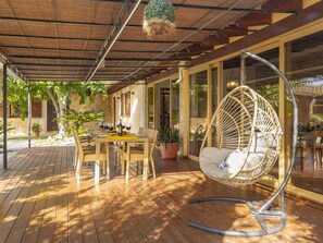 Une terrasse extérieure avec une table en bois, des chaises, un fauteuil suspendu et des plantes en pot.