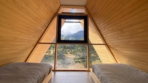 A triangular room with wooden walls and a large window at the top. There are two beds with gray bedding. - Outscape Cerro Castillo (Río Ibáñez)