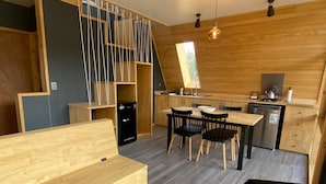A modern kitchen with wooden cabinets, a dining area with a wooden table and chairs, and a built-in bench. - Outscape Cerro Castillo (Río Ibáñez)