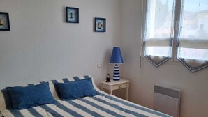 Ein Schlafzimmer mit einem Bett, einem Nachttisch, einer Lampe und einem Fenster.