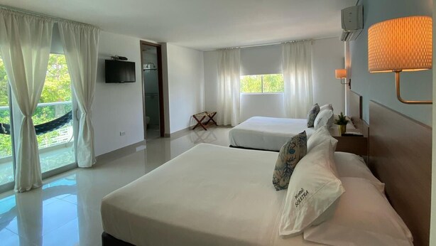 Une chambre d’hôtel avec un grand lit, deux petits lits, une télévision, une lampe et une vue sur la verdure.