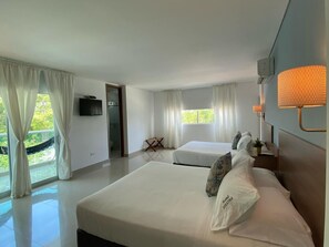 A hotel room with a large bed, two smaller beds, a TV, a lamp, and a view of greenery outside. - Hotel Soleira (Tolú)