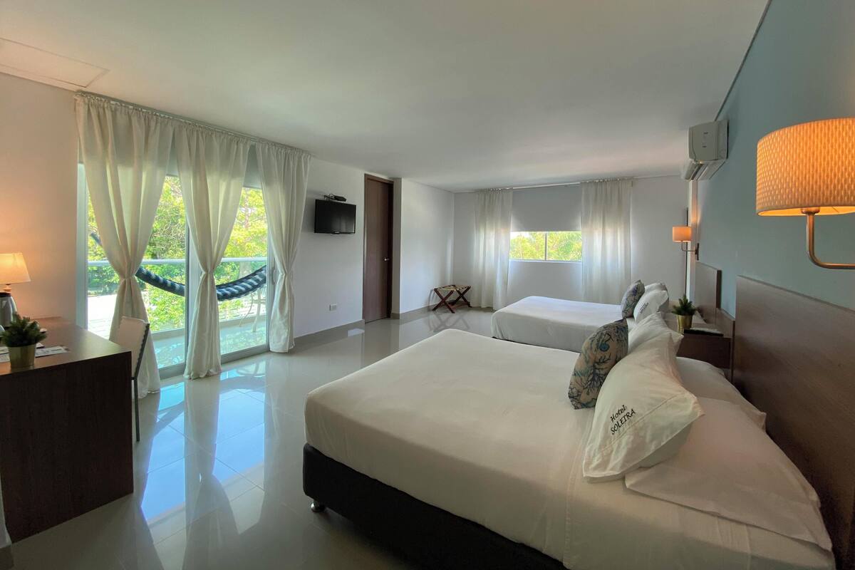A hotel room with a large bed, a desk, a TV, and a balcony with a hammock.