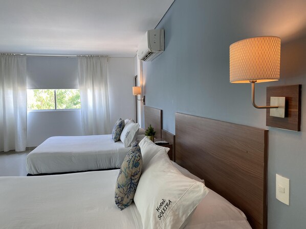A hotel room with two beds, a wall-mounted lamp, and a window with curtains. - Hotel Soleira (Tolú)