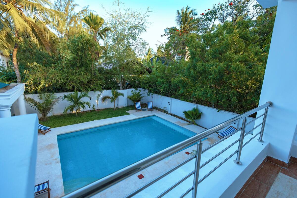 Ein Swimmingpool mit Metallgeländer, umgeben von üppiger Vegetation und Palmen.