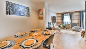 A dining area with a wooden table set for six, a fireplace, and a cozy seating area with a plant and a bean bag.