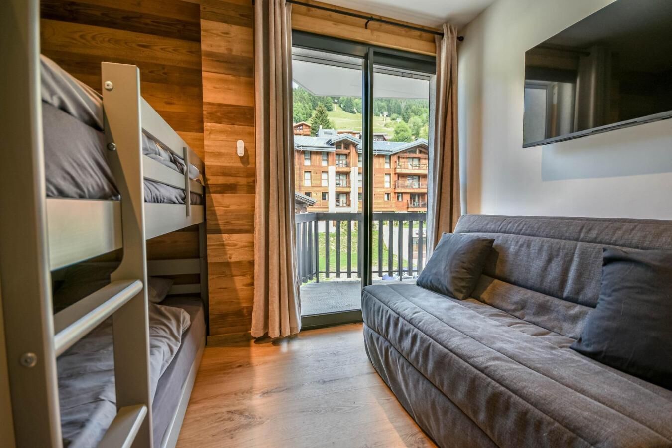 A room with bunk beds, a sofa, and a balcony with a view of buildings.