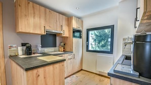 A modern kitchen with wooden cabinets, a black countertop, and a window providing a view of trees.
