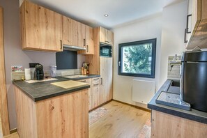 Een moderne keuken met houten kastjes, een zwart aanrechtblad en een raam met uitzicht op bomen.