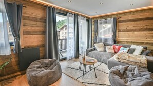 A modern living room with a sofa, two bean bags, a small table, and a view of a balcony with buildings in the background.