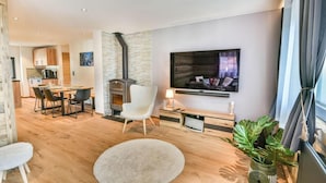 A modern living room with a fireplace, a dining area, and a kitchen in the background.