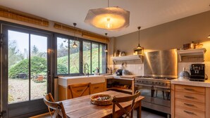A modern kitchen with a large island, stainless steel appliances, and large windows offering a view of the outdoors.