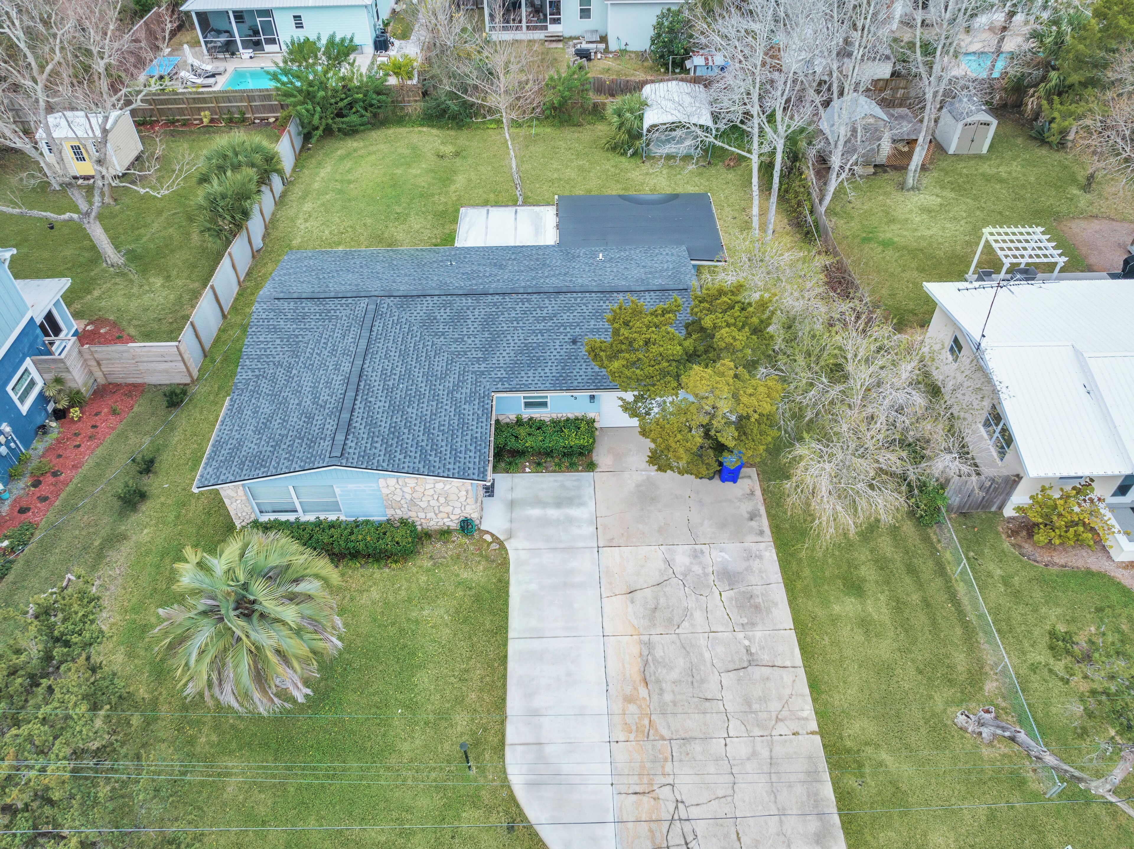 A residential property with a sloped roof, a front yard with a palm tree, and a driveway leading to the entrance.