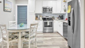 A modern kitchen with white cabinetry, stainless steel appliances, and a dining area with a glass table and patterned chairs.