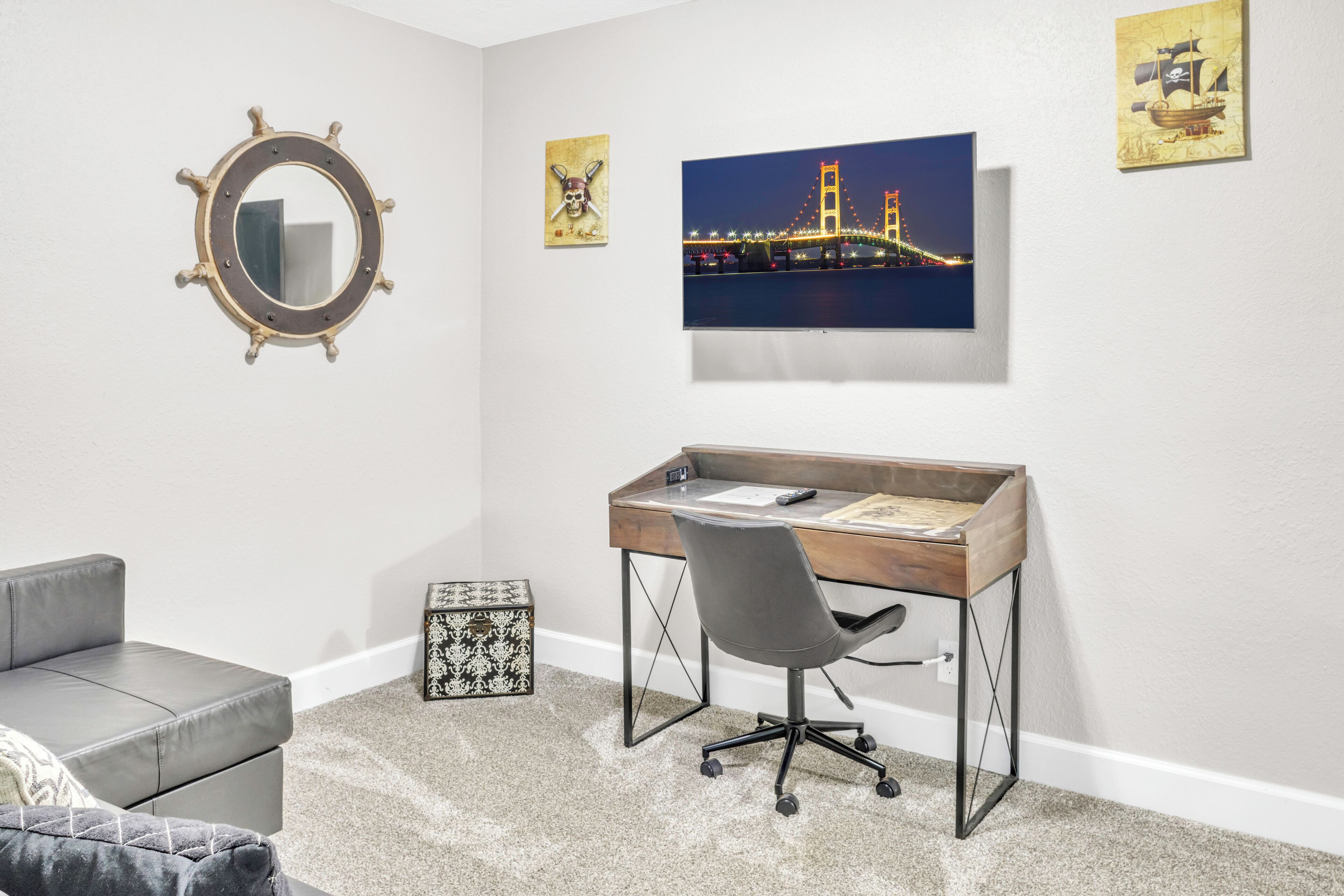 Ein Schlafzimmer mit einem Bett, einem Schreibtisch und einem Stuhl. An der Wand hängt ein Gemälde einer Brücke.