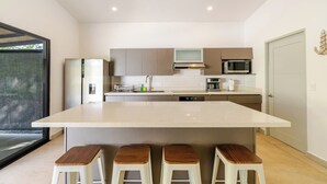 A modern kitchen with a central island, bar stools, and a view of the outdoors.