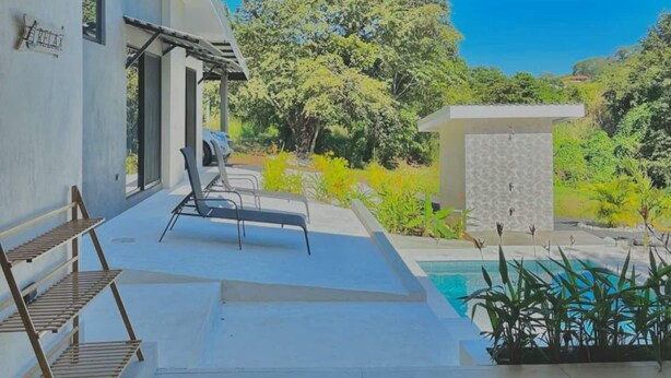 A covered outdoor area with a pool, lounge chairs, and a pergola.
