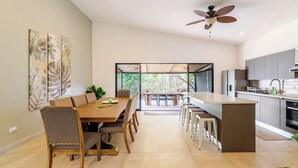 A modern kitchen with a central island, a dining area with a wooden table and chairs, and a ceiling fan.