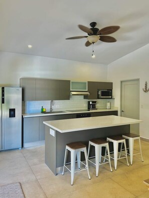 Una cocina moderna con una isla central, taburetes de bar, ventilador de techo y electrodomésticos integrados.