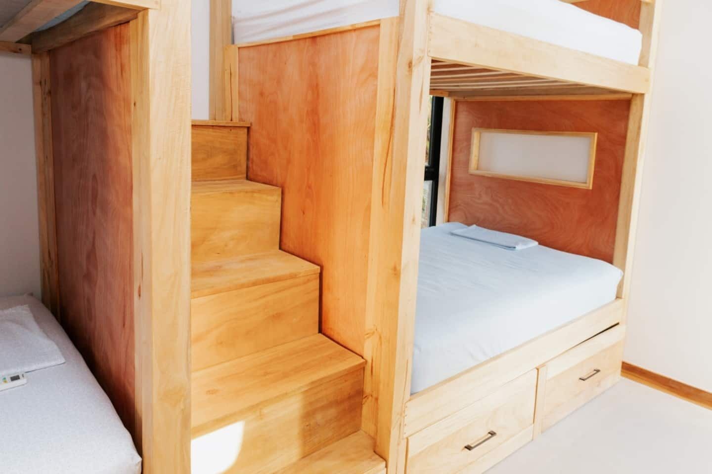 A bunk bed with a wooden staircase and a single bed.