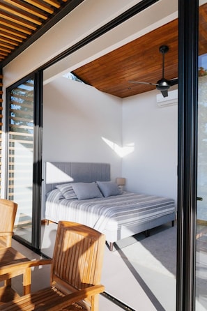 Un dormitorio moderno con una cama, techo de madera y vistas a través de un ventanal.