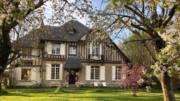 Ein traditionelles Fachwerkhäuschen mit Steinaußenwand, einer Veranda mit zwei Stühlen und einem gepflegten Rasen.