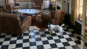 Ein Zimmer mit kariertem Boden, zwei braunen Ledersesseln, einem runden Couchtisch und einem weißen Hund.