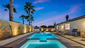A swimming pool with a stone wall and palm trees, a barbecue grill, and outdoor seating. - NEW Lush Luxury Living-Heated Pool/Spa Included. Walking distance to Coachella (Indio)