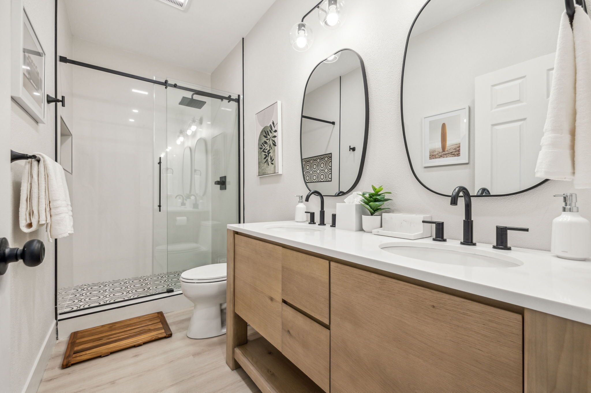 A modern bathroom with a glass-enclosed shower, a white sink with black faucets, and wooden cabinets.
